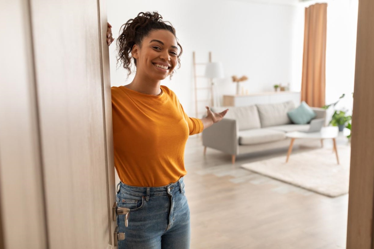 A happy woman stands at the door of her new home, after a great customer experience with her home builder.