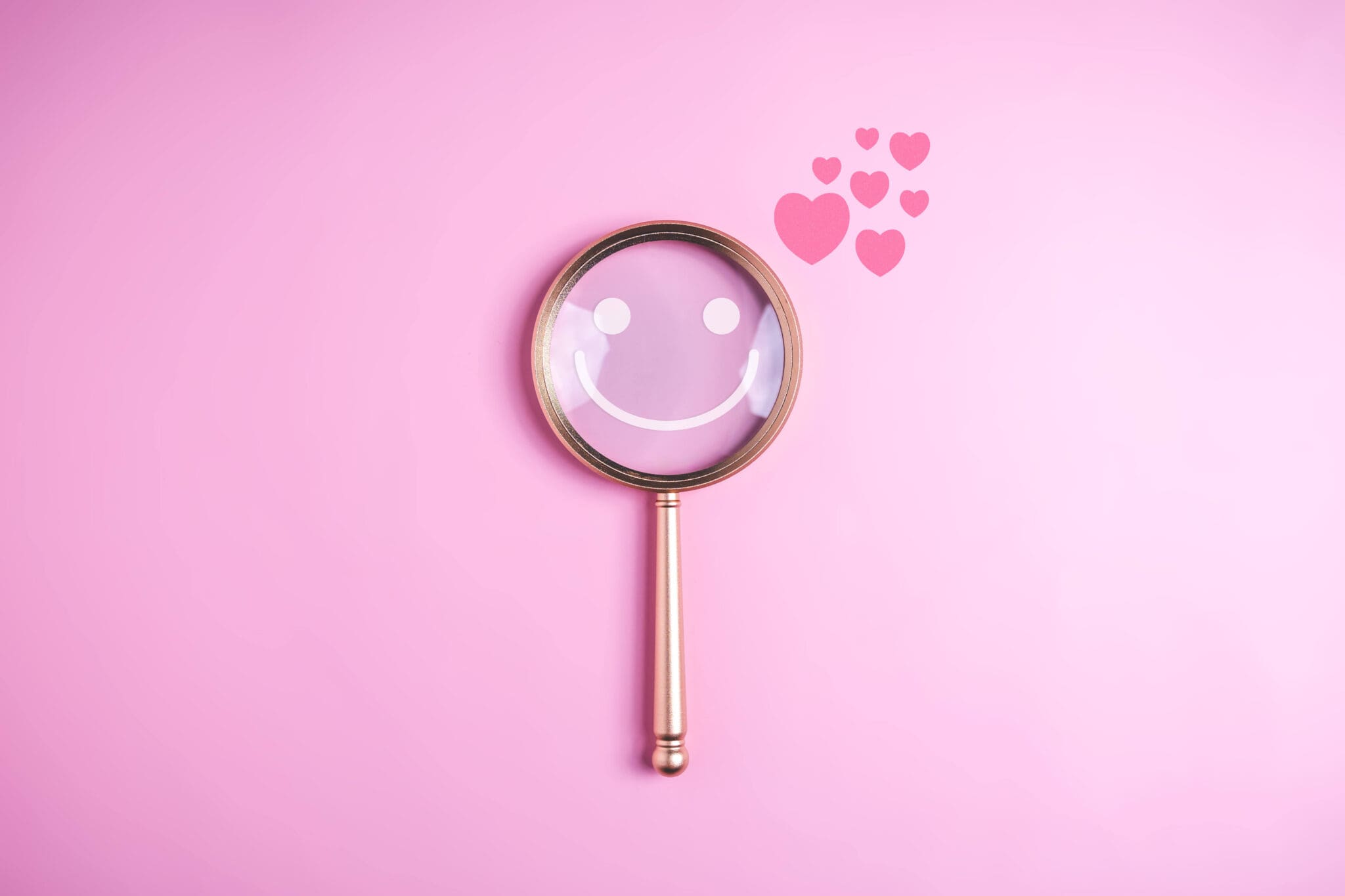 Magnifying glass with hearts on a pink background, representing reviews and searchability