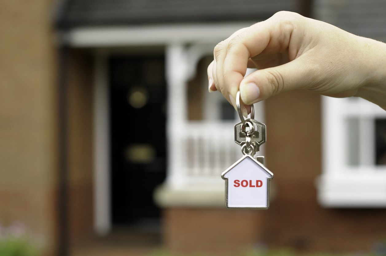 Keys and a sold sign hang in front of new home, illustrating successful home builder marketing.