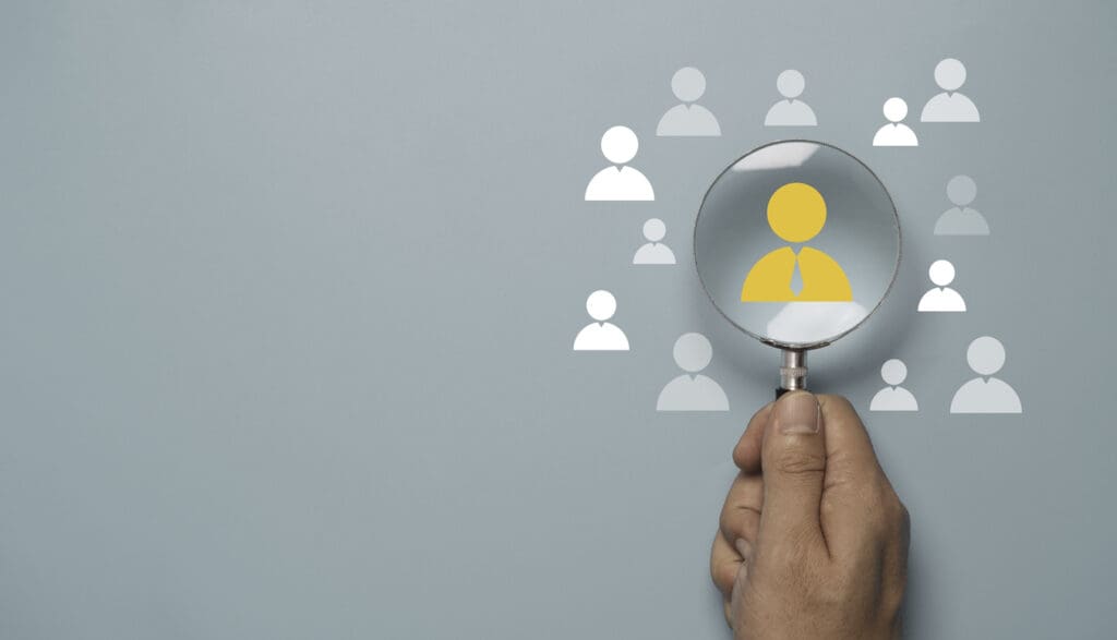 Hand holding magnifying glass over human icons shows how AI can help identify customer intent.