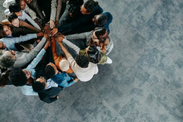 A homebuilder team touches hands in a circle to show their teamwork and effective workforce management.