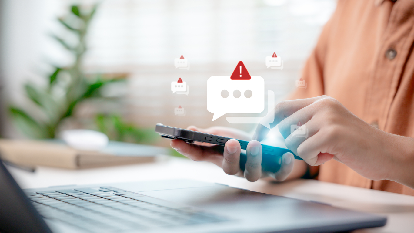 Person checks messages on their phone with red alarm signs floating to represent the risks of sending non-compliant SMS messages. 