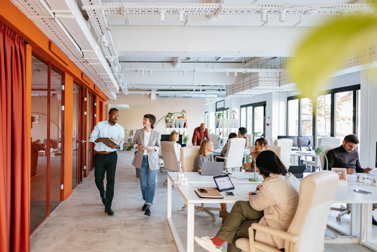 An open office with people working shows how some real estate firms are cutting overhead costs by changing office space and layout. 
