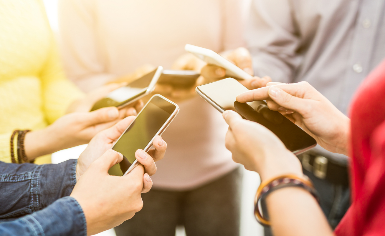A group of people holding their phones in a circle illustrates the need for personalized SMS mass texting. 
