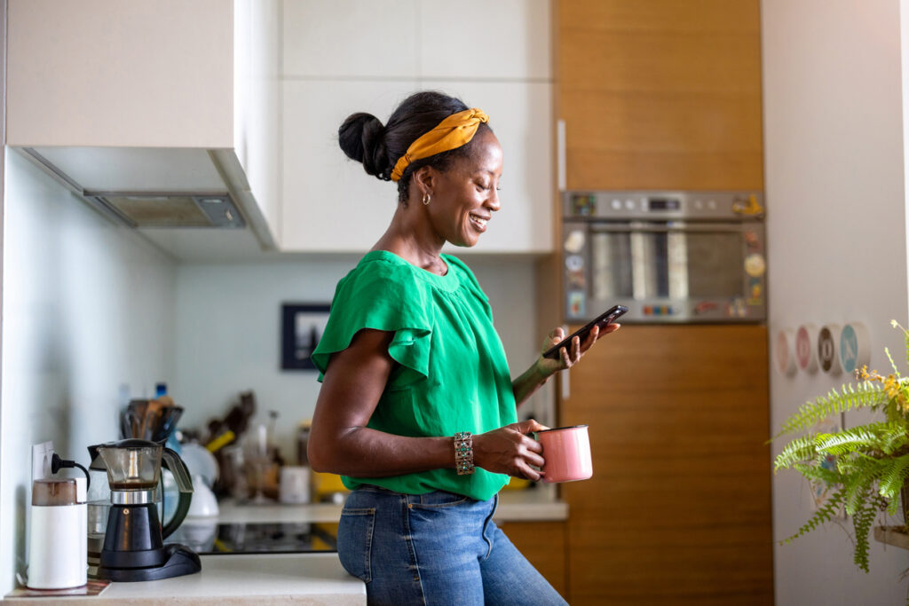 Happy woman leans against her kitchen counter and reads a personalized mass text from her phone.