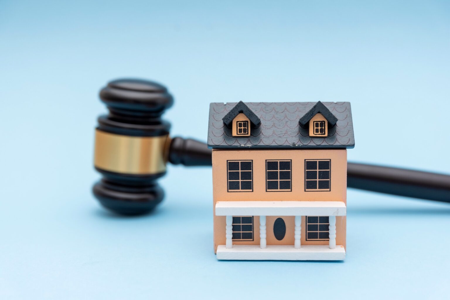 Small house model and judge gavel on blue background, representing TCPA compliance for mortgage