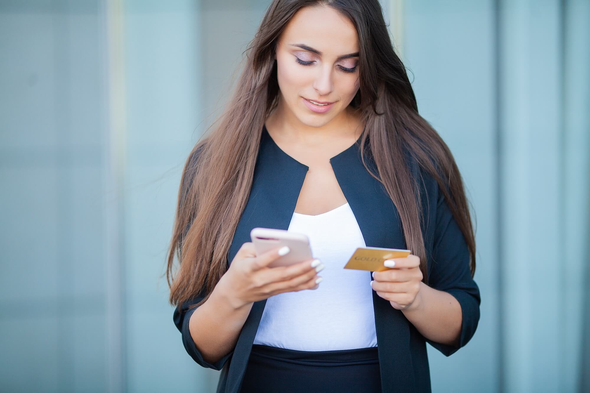 Woman uses mobile messaging while looking at credit card
